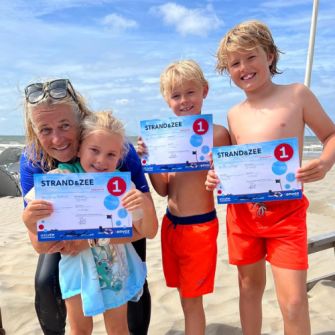 Kinderen op het strand die een erkend ENVOZ-diploma vasthouden na de Swim Fun Safe Sea Clinic te hebben gedaan